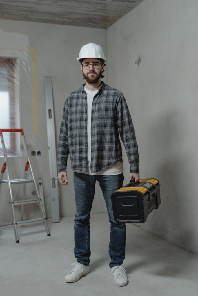 a-man-carrying-a-tool-box-6474460 Construction worker in plaid shirt with toolbox indoors, showcasing renovation setting.